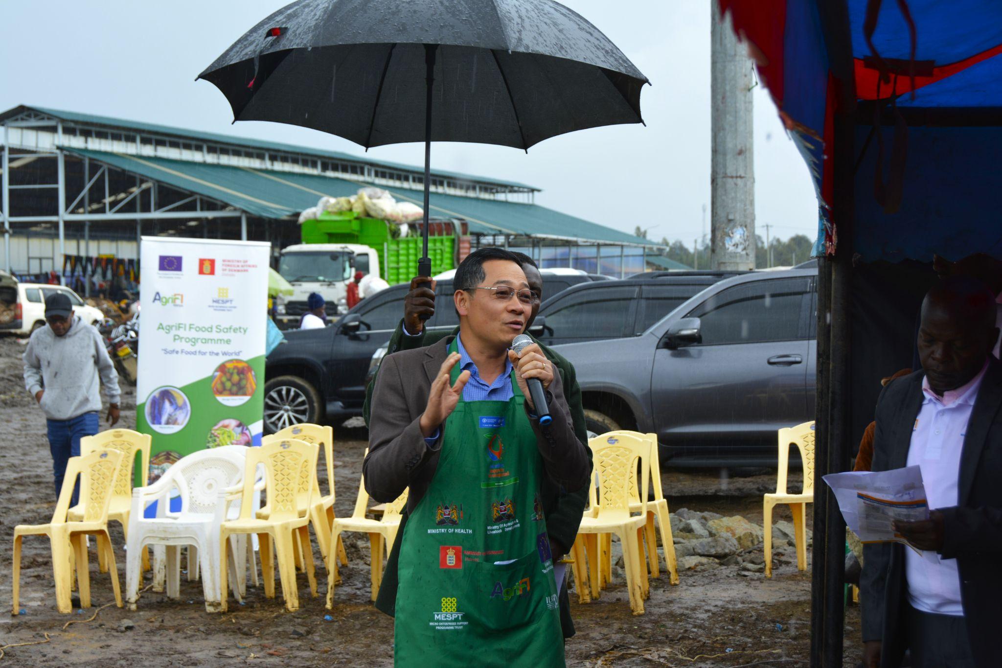 A person holding an umbrella and talking into a microphone</p>
<p>Description automatically generated